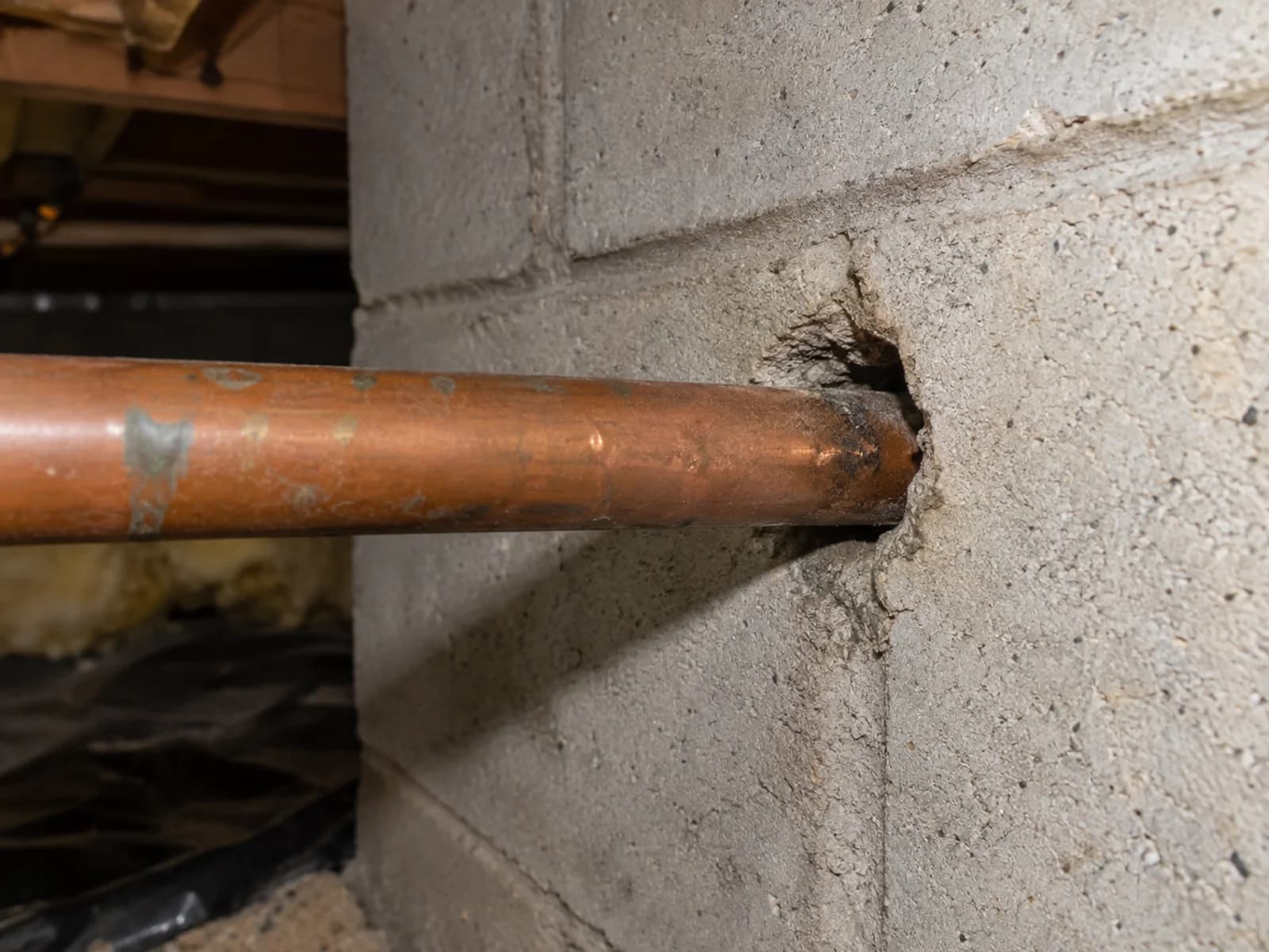 Dime-sized gap where a copper pipe passes through a block foundation.